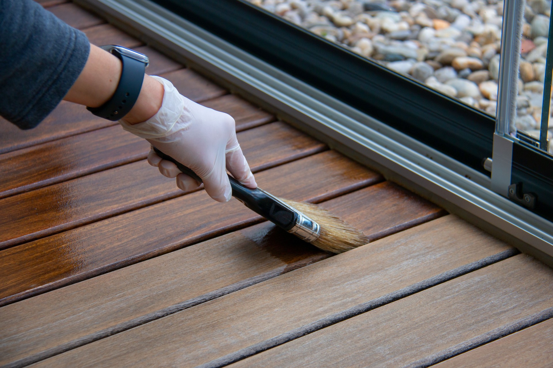 Deck staining, worker hand applying deck oil on decking boards with paint brush