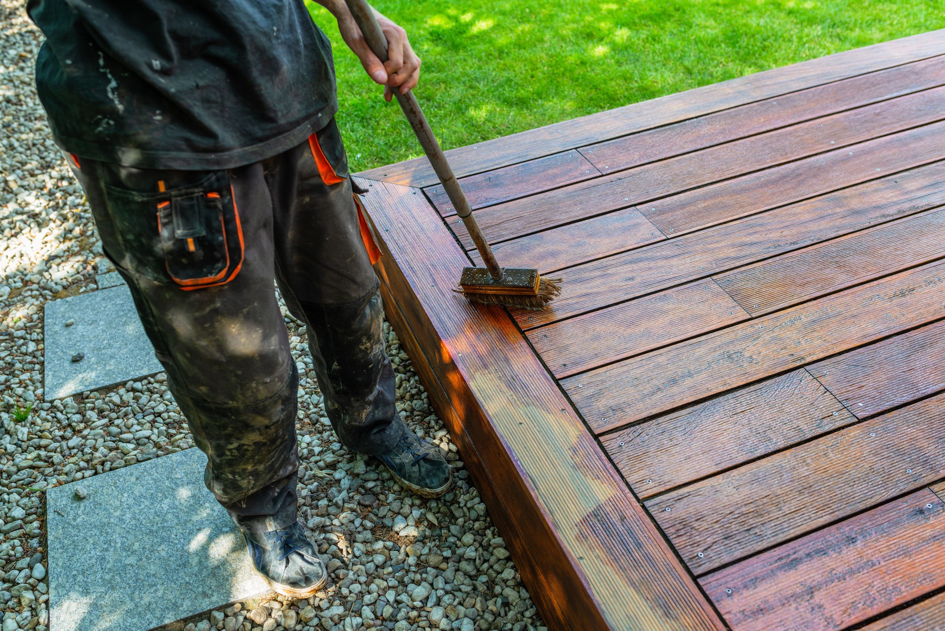 Close-up of a wooden deck being stained with a brush for protection and maintenance